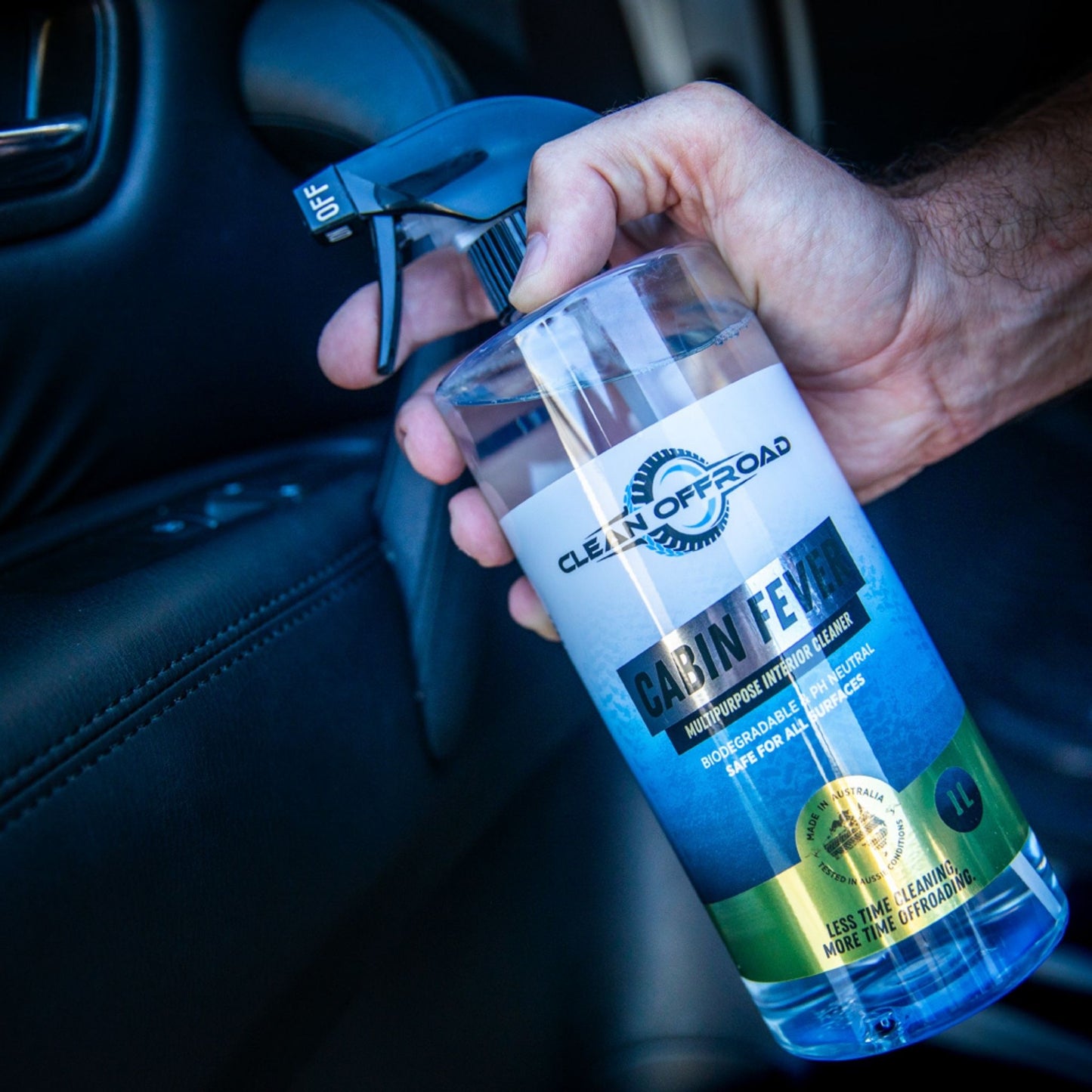 Hand holding a bottle of 'Cabin Fever' interior cleaner inside a car.