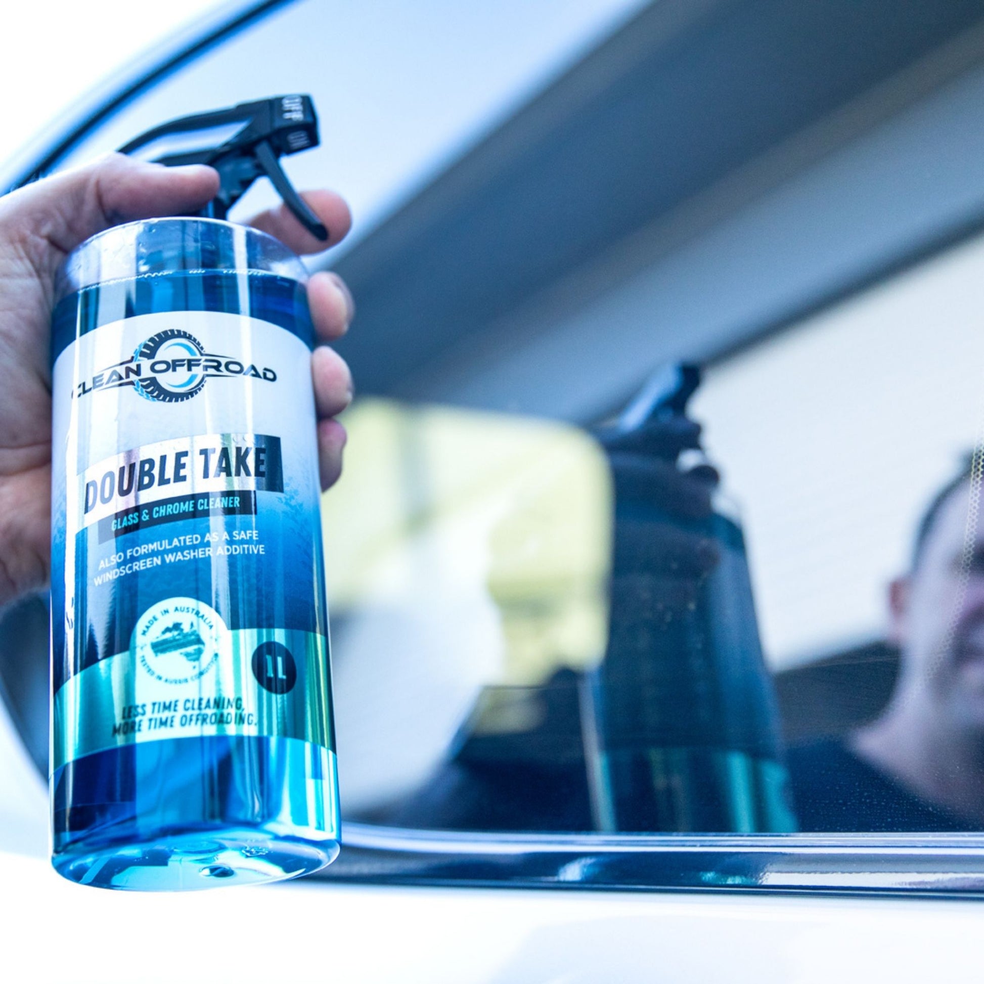 Person holding a bottle of 'Double Take' glass cleaner inside a vehicle.